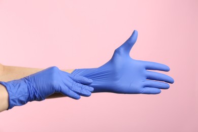 Photo of Person putting on medical gloves against pink background, closeup of hands