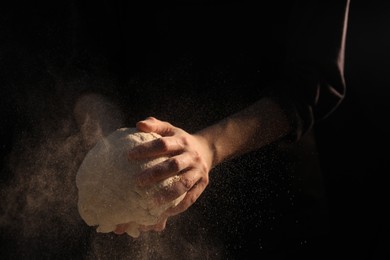 Photo of Making bread. Woman kneading dough on dark background, closeup