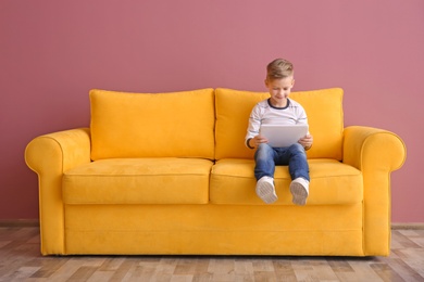 Photo of Cute little boy sitting on sofa with tablet computer, indoors