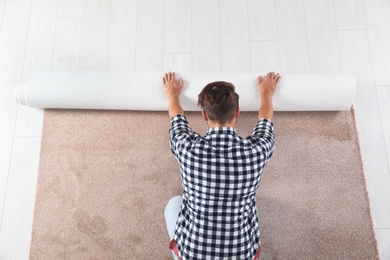 Photo of Man rolling out new carpet flooring indoors, top view