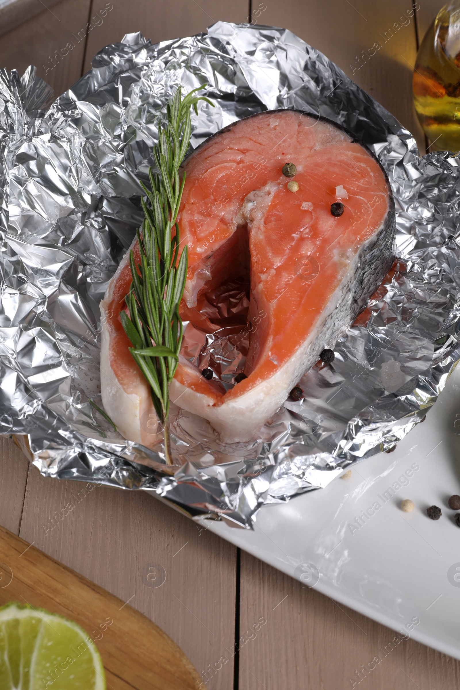 Photo of Aluminum foil with raw salmon, rosemary and spices on wooden table