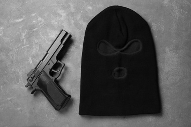Photo of Black knitted balaclava and pistol on grey table, flat lay
