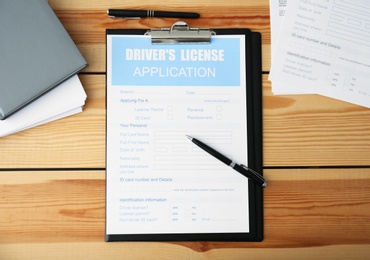 Driver's license application form, documents and stationery on wooden table, flat lay