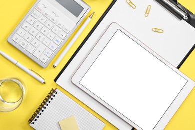Photo of Modern tablet, stationery and glass of water on yellow background, flat lay. Space for text