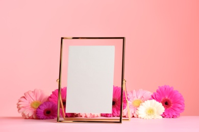 Photo of Stylish photo frame and beautiful flowers on table against color background, space for text