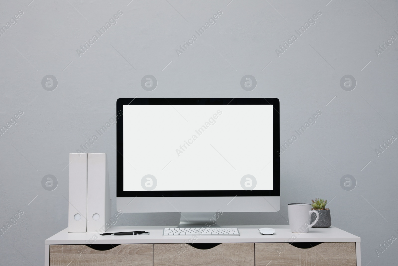 Photo of Comfortable workplace with blank computer display on desk near light grey wall. Space for text