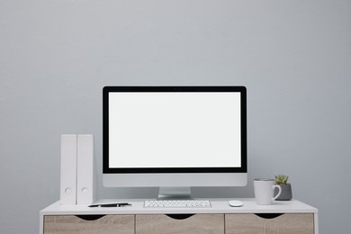 Photo of Comfortable workplace with blank computer display on desk near light grey wall. Space for text