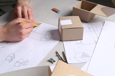 Man creating packaging design at light wooden table, closeup