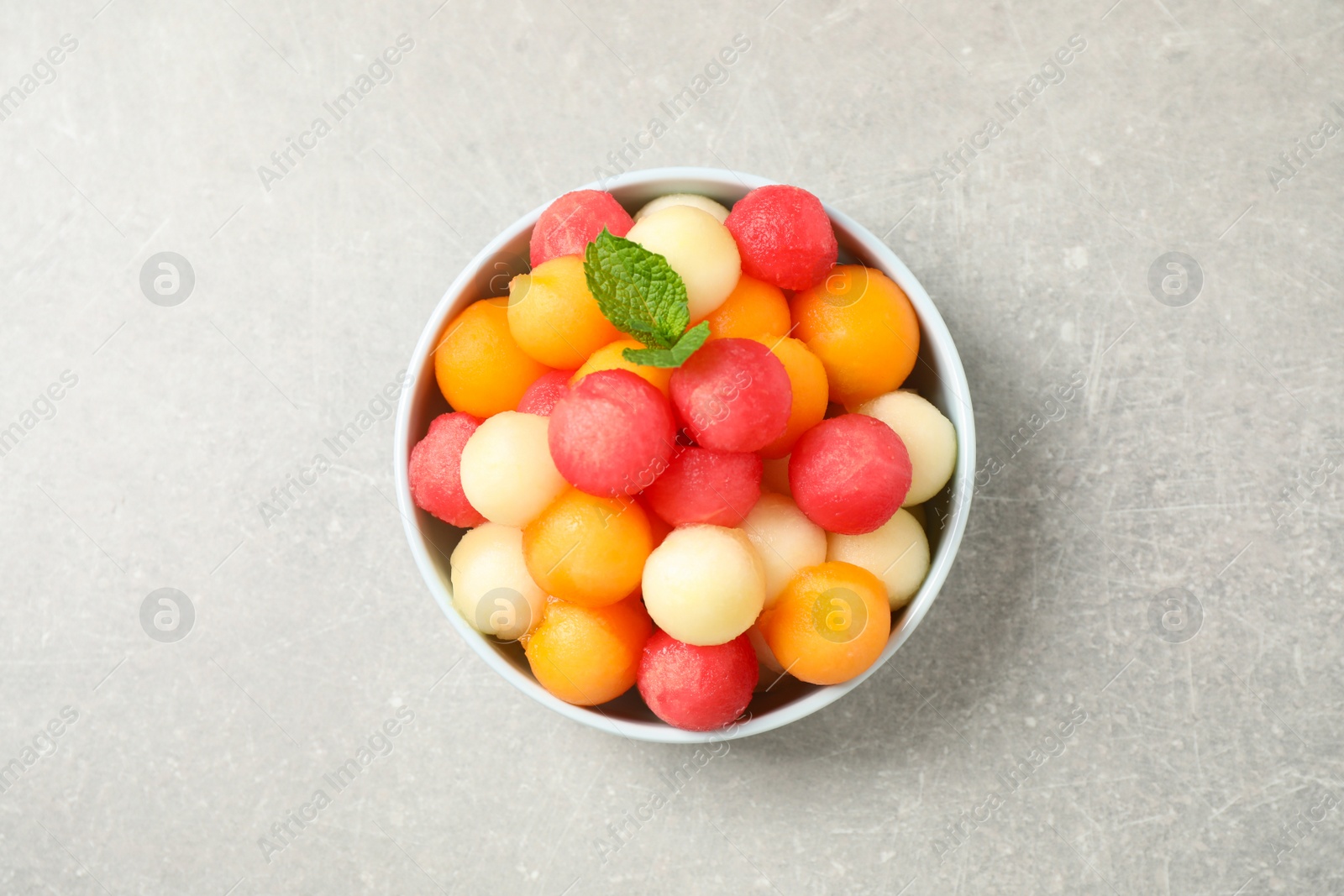 Photo of Melon balls and mint in bowl on grey table, top view