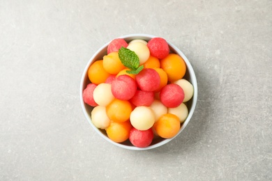 Melon balls and mint in bowl on grey table, top view