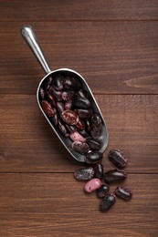 Photo of Metal scoop with dry kidney beans on wooden table, flat lay