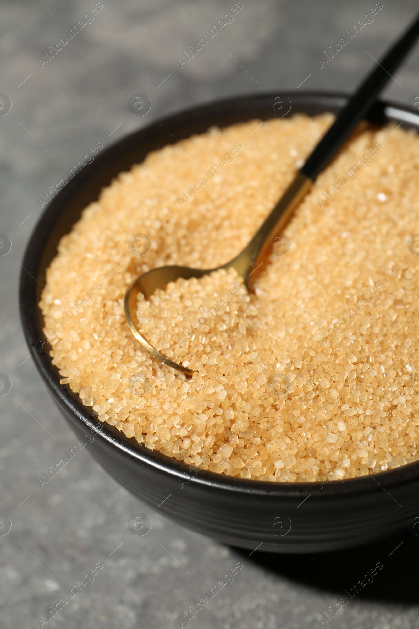 Photo of Brown sugar in bowl and spoon on grey textured table, closeup