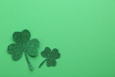 St. Patrick's day. Shiny decorative clover leaves on green background, flat lay. Space for text