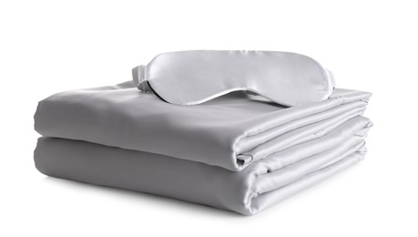 Photo of Stack of clean silky bed linen and sleeping mask isolated on white