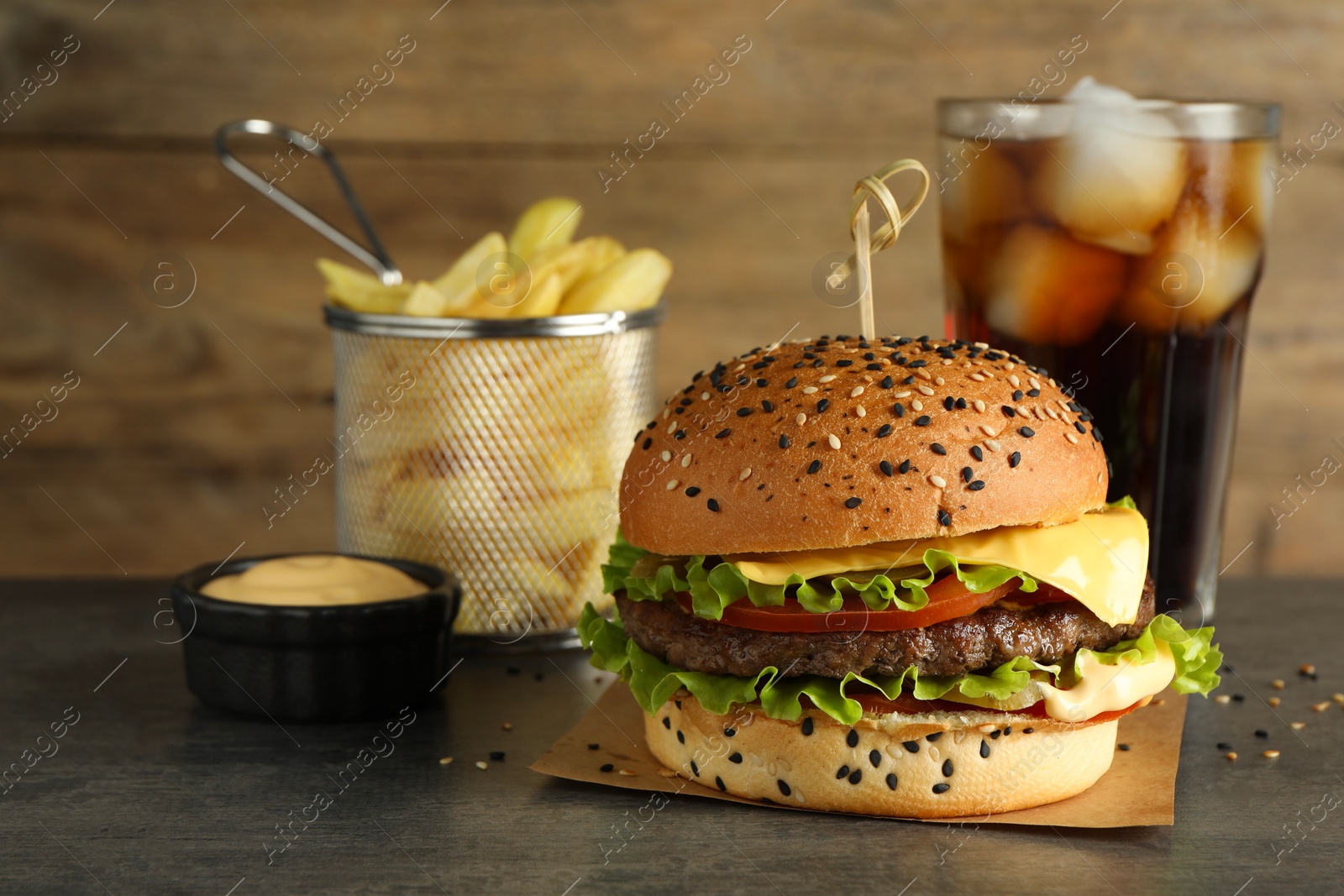 Photo of Burger with delicious patty, soda drink, french fries and sauce on gray table
