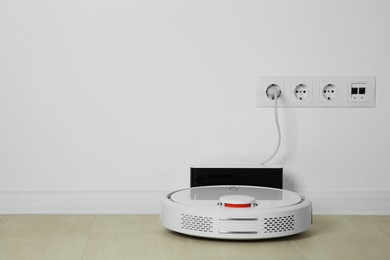 Photo of Robotic vacuum cleaner charging from electric socket on floor indoors. Space for text