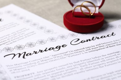 Marriage contract and golden wedding rings on grey table, closeup