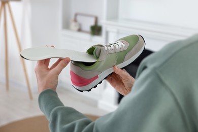 Photo of Woman putting orthopedic insole into shoe at home, closeup. Foot care