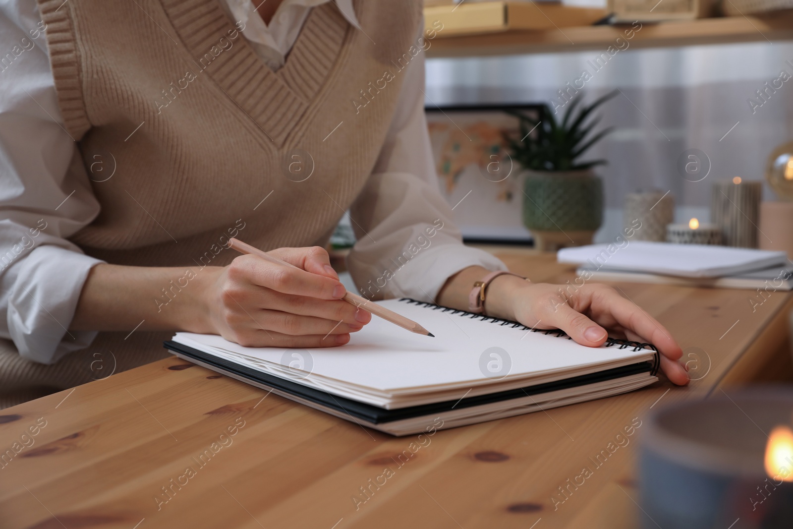 Photo of Woman drawing in sketchbook with pencil at wooden table indoors, closeup