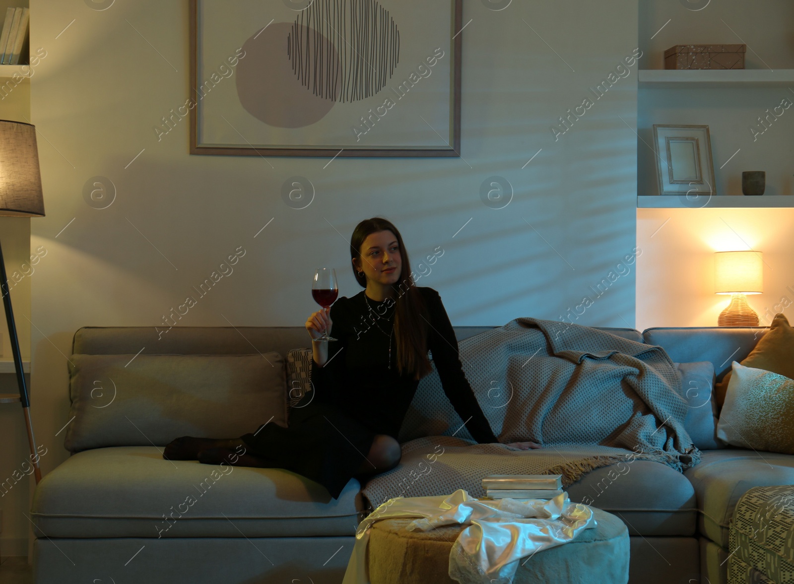 Photo of Woman with glass of wine resting on couch in room at night