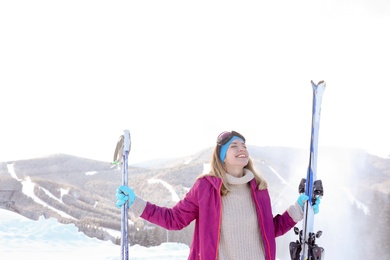 Happy young woman with ski equipment spending winter vacation in mountains. Space for text