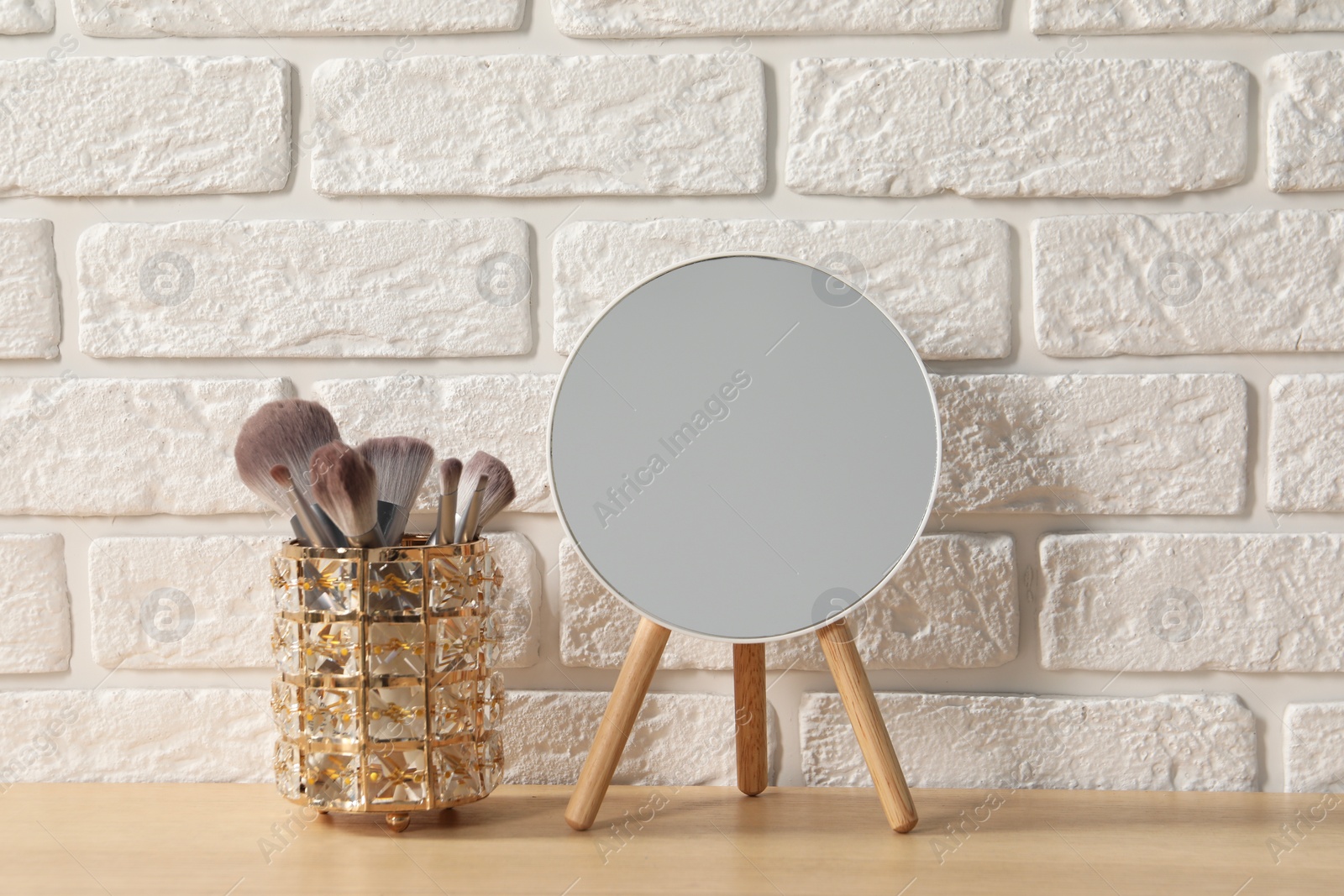 Photo of Mirror and makeup brushes on wooden dressing table in room