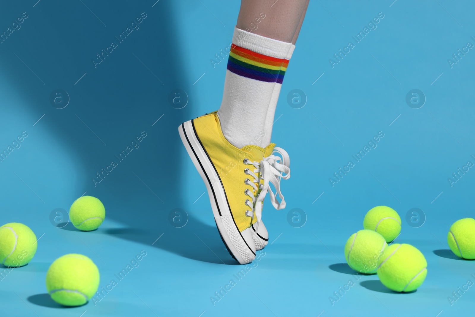 Photo of Woman posing in yellow classic old school sneakers and tennis balls on light blue background, closeup