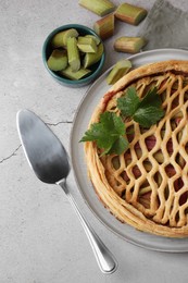 Photo of Freshly baked rhubarb pie, cut stalks and cake server on light grey table, flat lay
