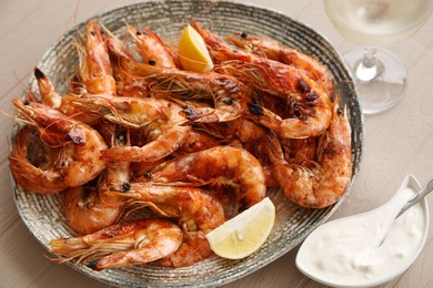 Photo of Plate of delicious cooked shrimps served with lemon, sauce and wine at table, closeup