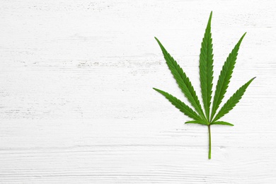 Photo of Leaf of medical hemp on white wooden background, top view. Space for text