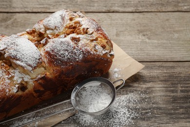 Delicious yeast dough cake and strainer with powdered sugar on wooden table