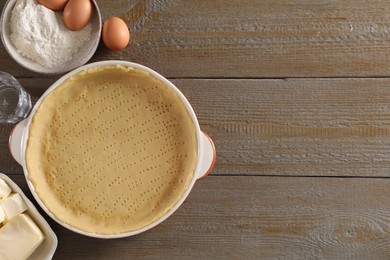 Photo of Making quiche. Baking dish with fresh dough and ingredients on wooden table, flat lay. Space for text