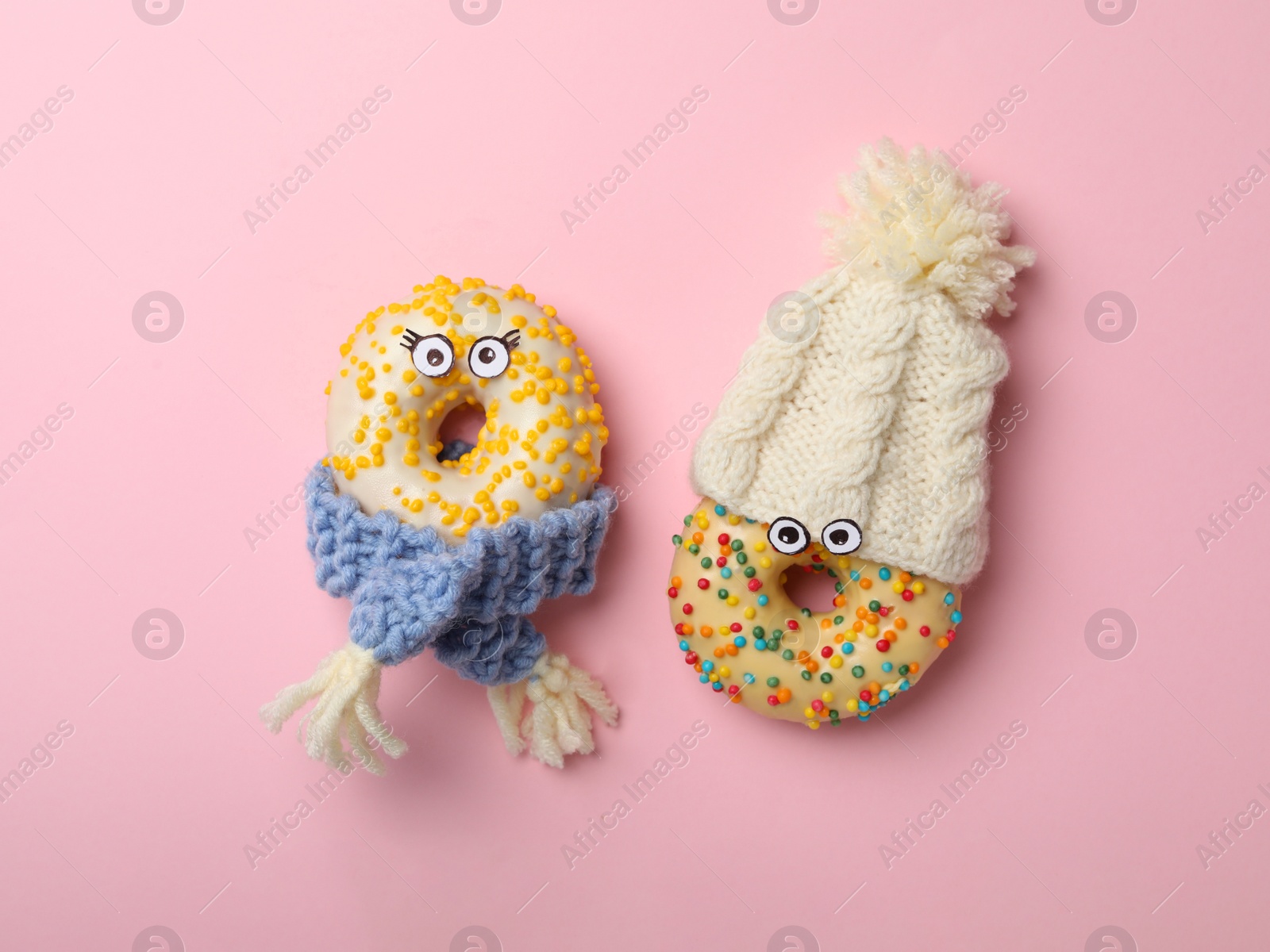 Photo of Funny faces made with donuts and warm clothes on pink background