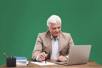 Portrait of senior teacher with laptop at table against green chalkboard