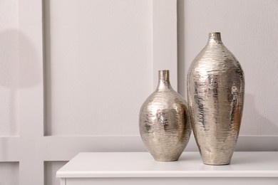Photo of Shiny vases on white table indoors, space for text. Interior element