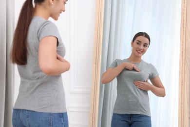 Beautiful happy woman doing breast self-examination near mirror indoors