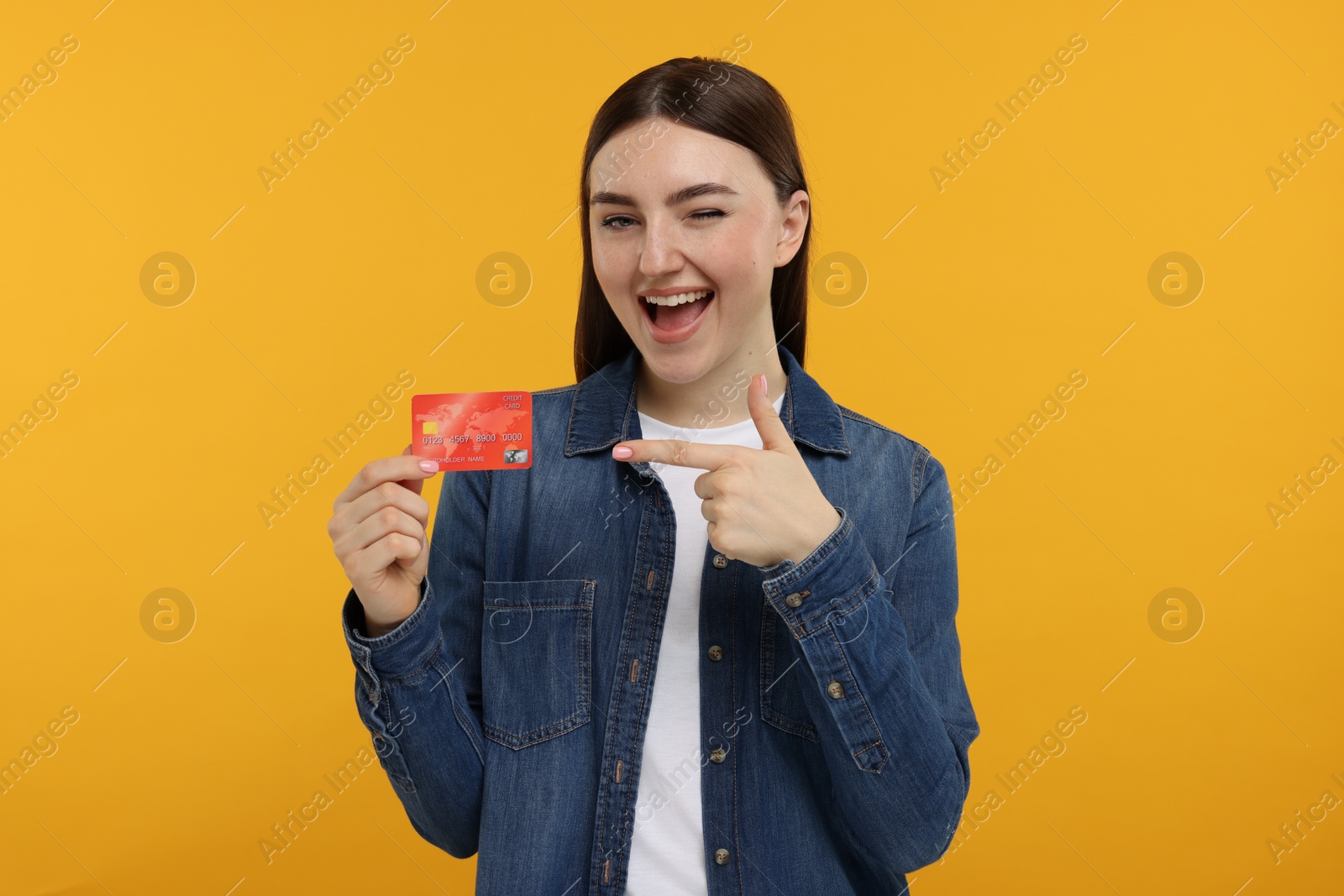 Photo of Happy woman pointing at credit card on orange background