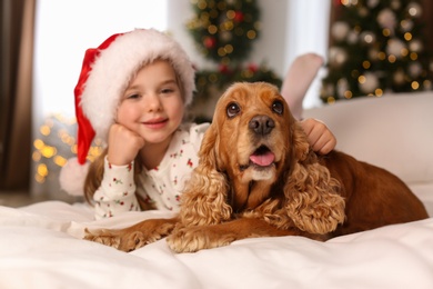 Photo of Cute little girl with English Cocker Spaniel on bed in room decorated for Christmas