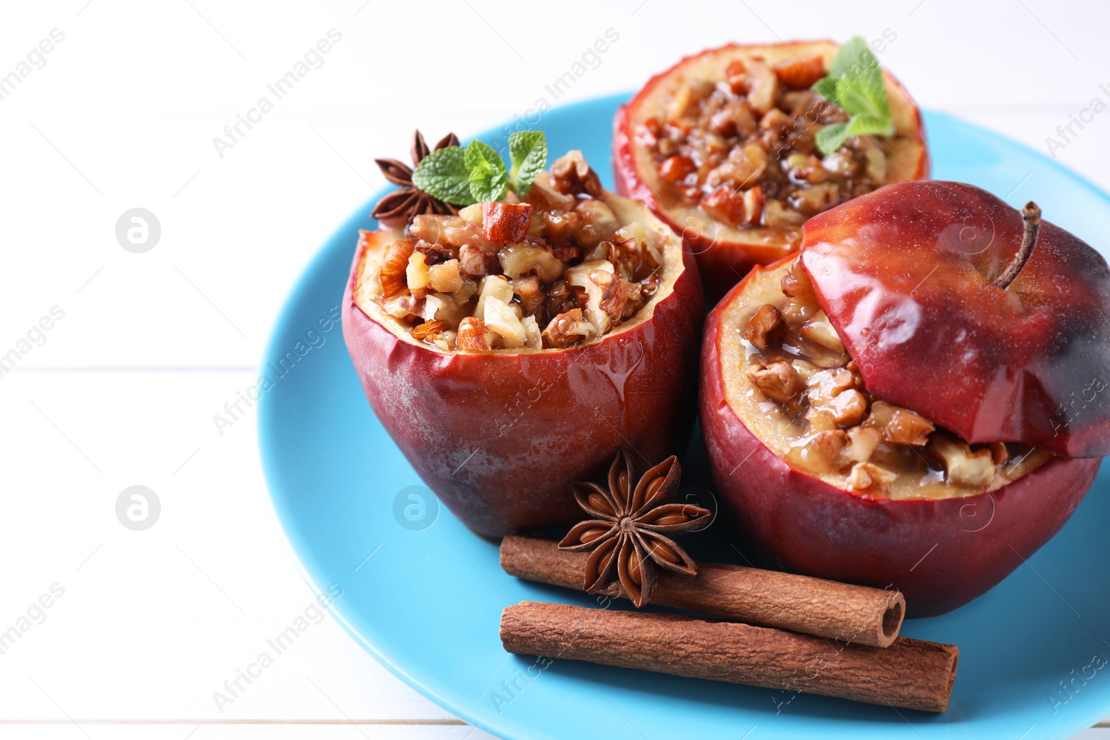 Photo of Tasty baked apples with nuts, honey, spices and mint on white wooden table, closeup