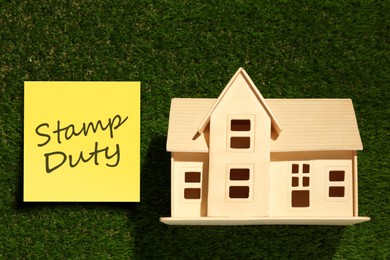 Image of Wooden house model ans sticky note with text Stamp Duty on green grass, top view