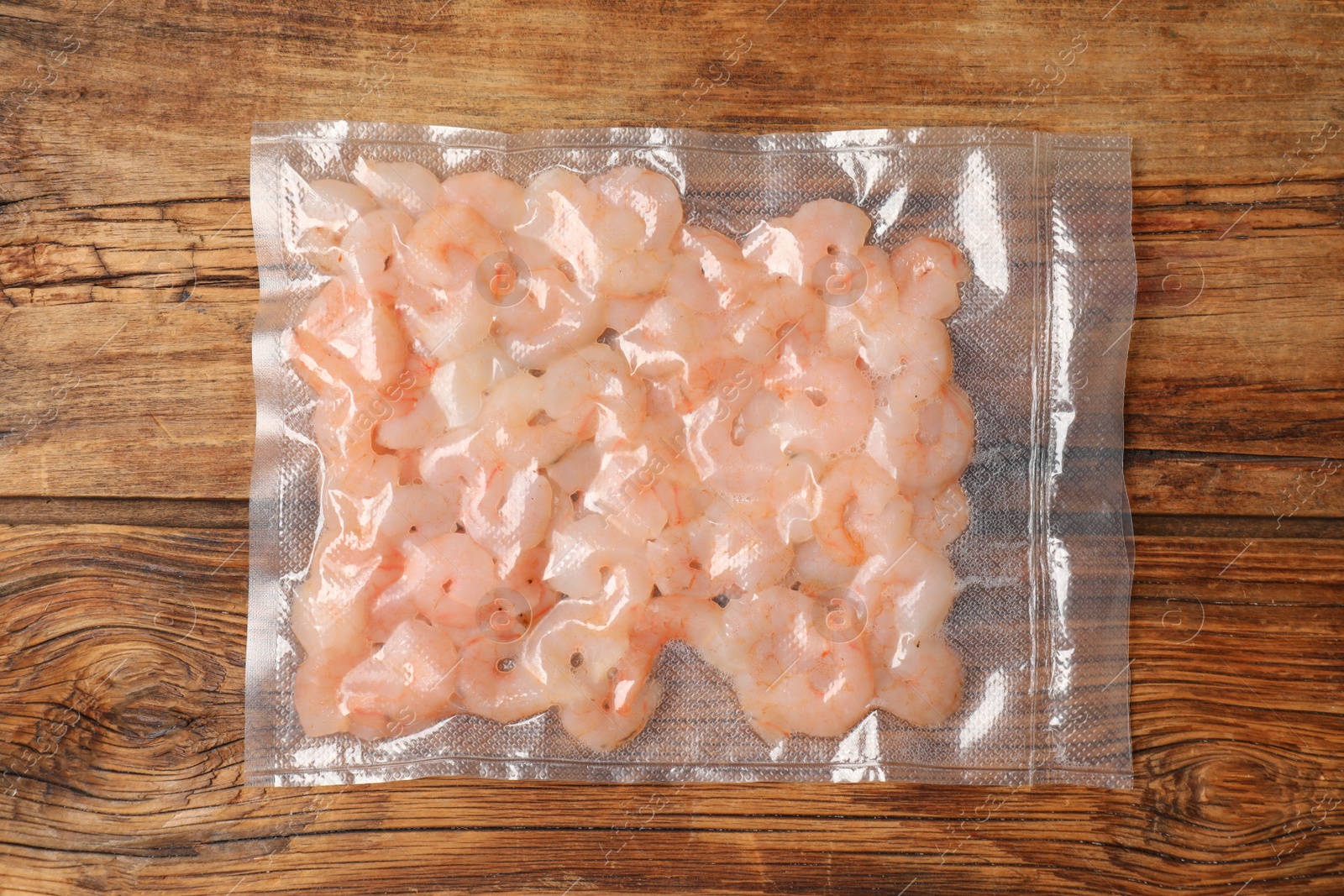 Photo of Vacuum pack of shrimps on wooden table, top view