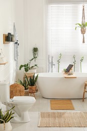 Stylish white tub and green houseplants in bathroom. Interior design