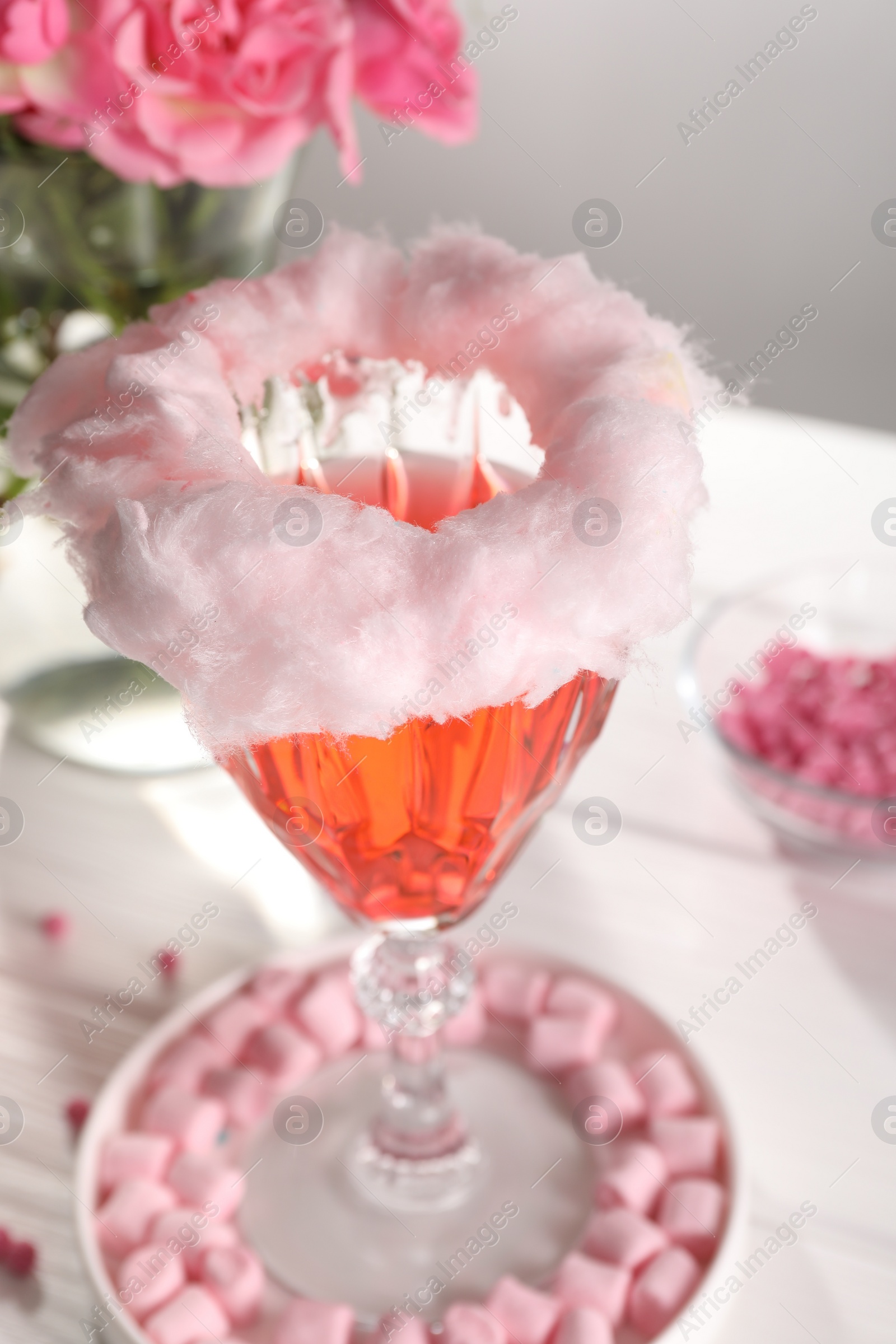 Photo of Cotton candy cocktail in glass and marshmallows on white table, closeup