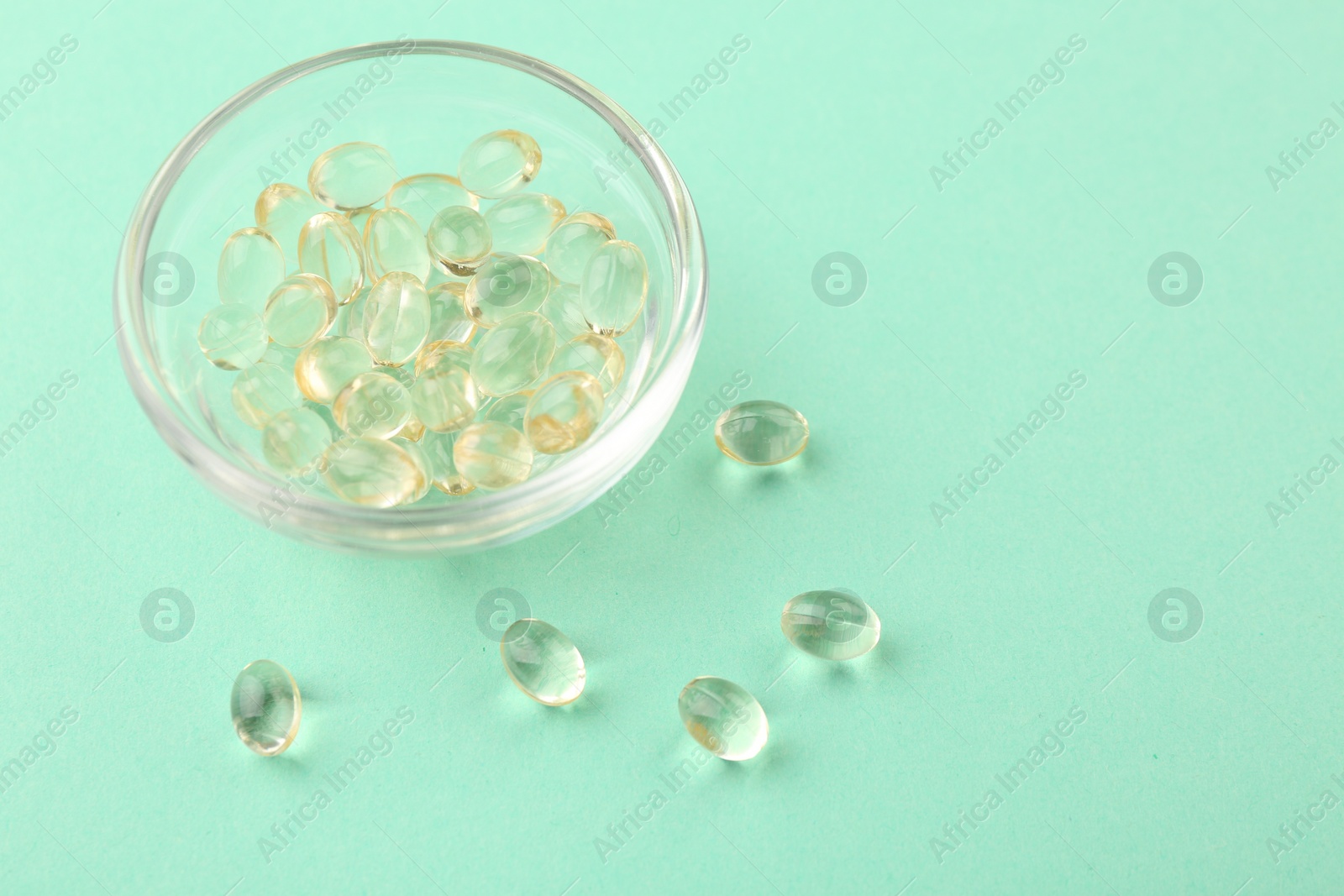 Photo of Vitamin capsules in glass bowl on turquoise background, closeup. Space for text