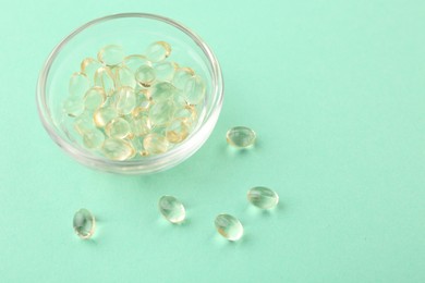Photo of Vitamin capsules in glass bowl on turquoise background, closeup. Space for text