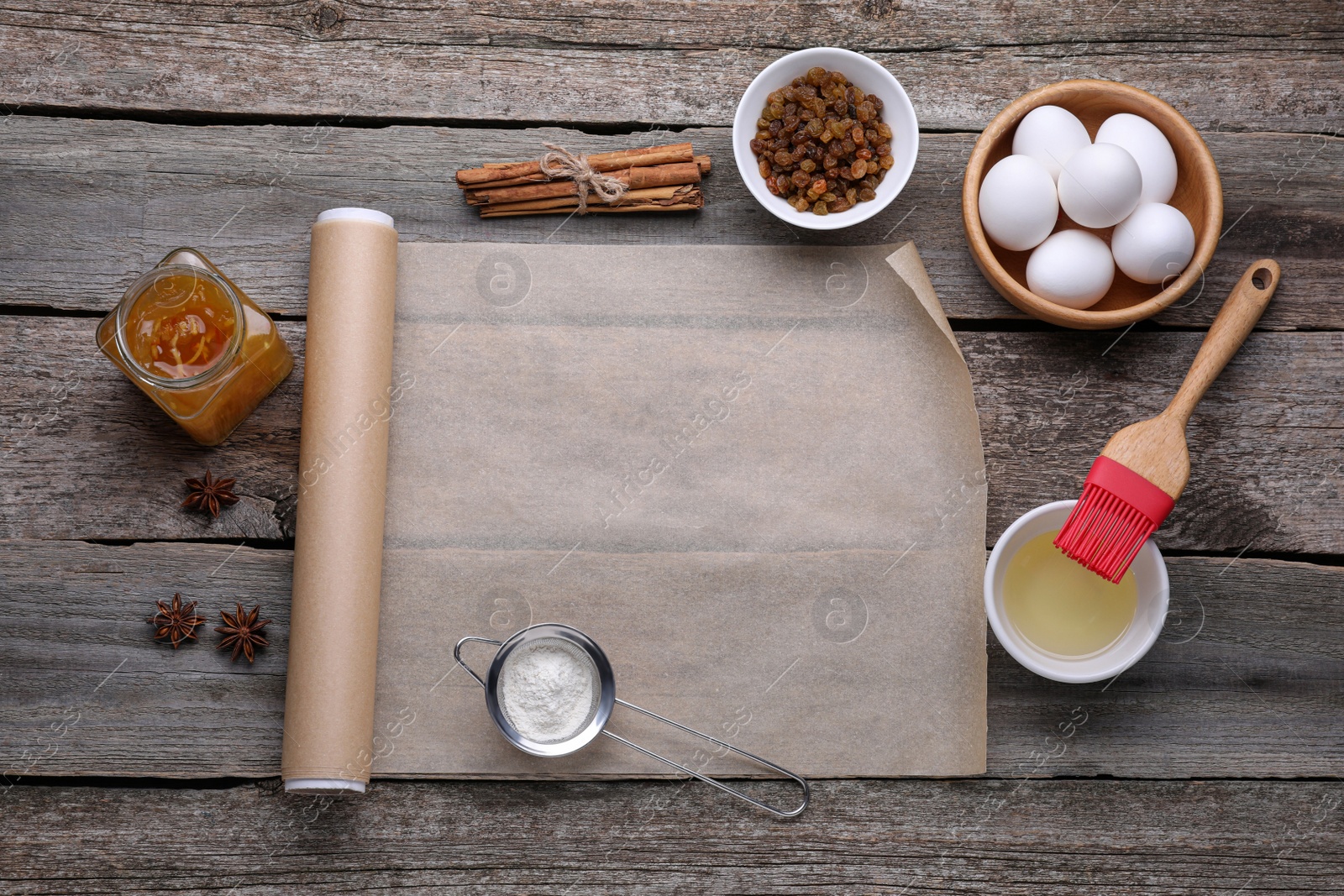 Photo of Roll of baking parchment paper, different ingredients and kitchen tools on wooden table, flat lay. Space for text