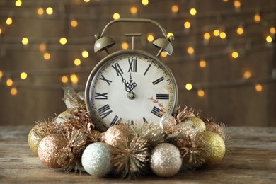 Vintage alarm clock with decor on wooden table against blurred Christmas lights. New Year countdown