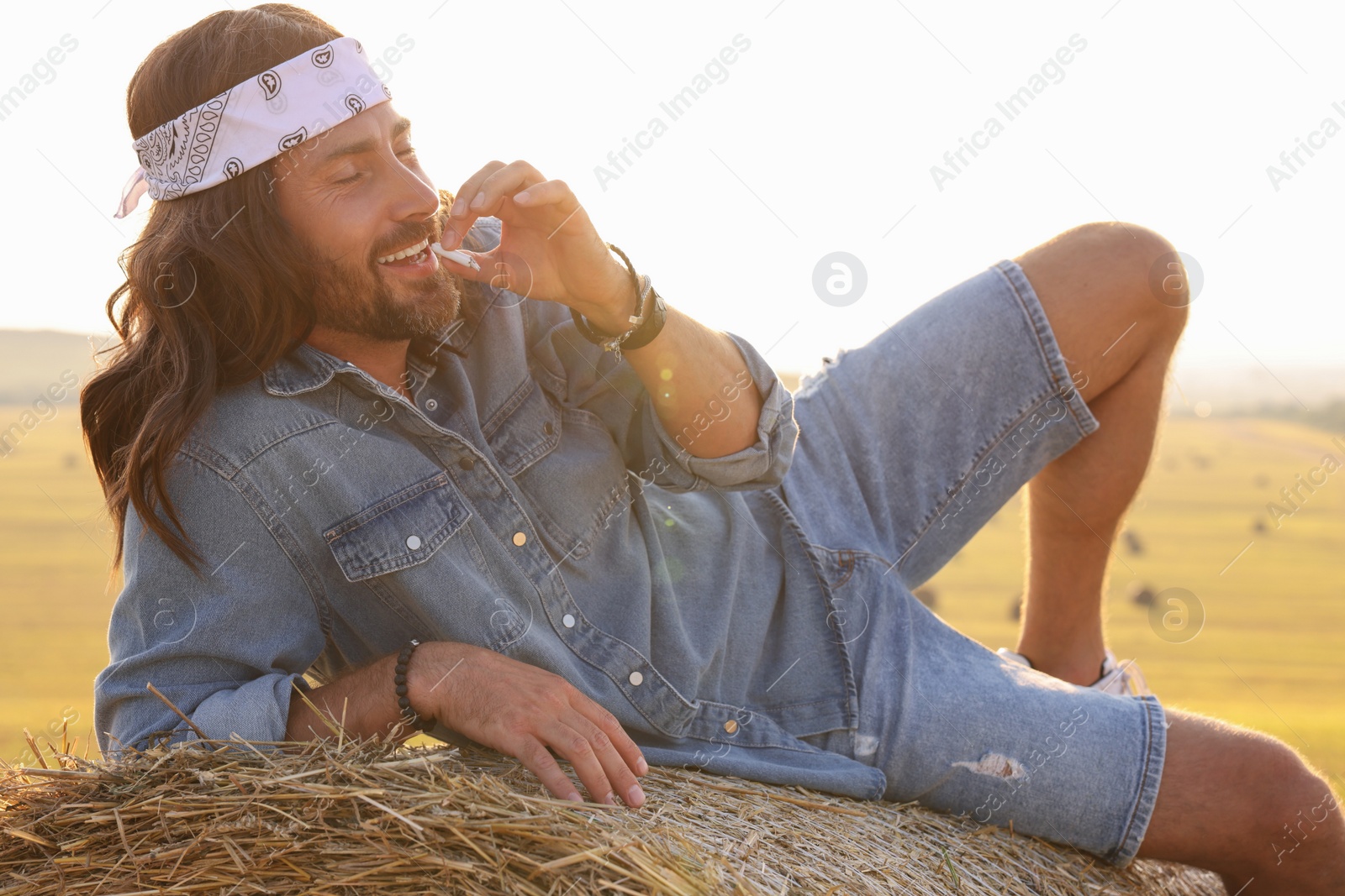 Photo of Hippie man smoking joint on hay bale in field