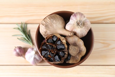 Bulbs of fresh and fermented black garlic on wooden table, flat lay