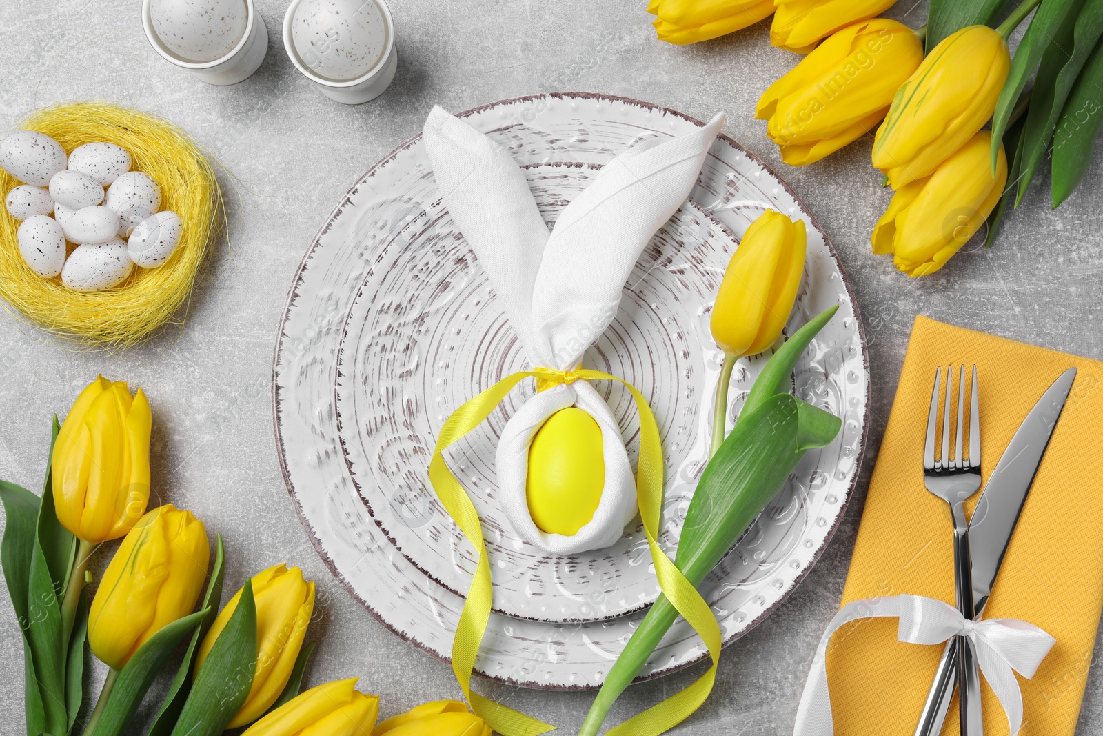 Photo of Festive table setting with bunny made of painted egg and napkin on light grey background, flat lay. Easter celebration